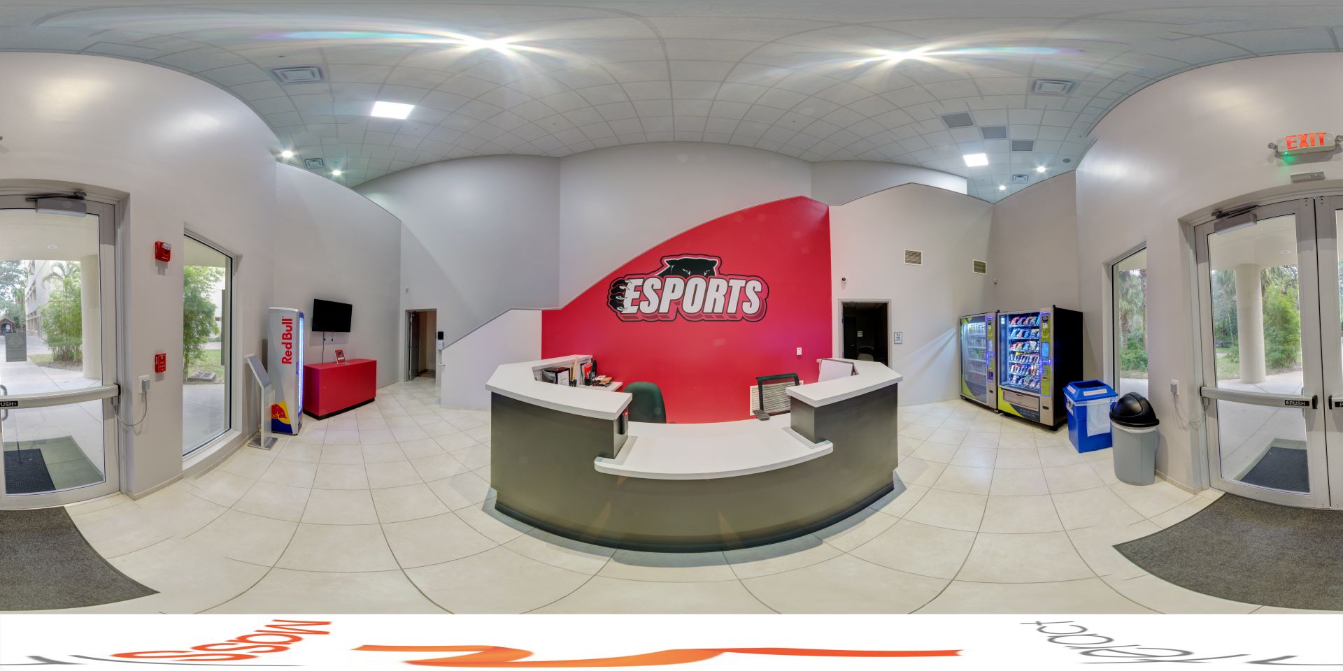Panoramic view of the Esports center lobby with a reception desk in the center, vending machines on the right, and doors leading outside on both sides